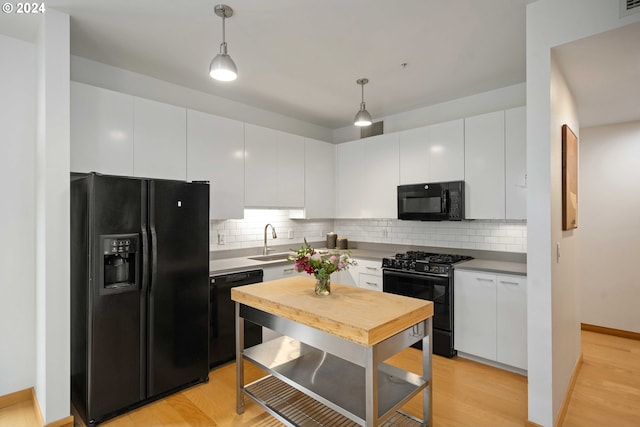 kitchen featuring white cabinets, light wood-type flooring, hanging light fixtures, and black appliances