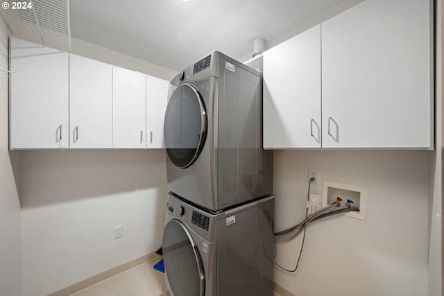 clothes washing area featuring stacked washer and clothes dryer and cabinets