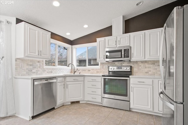 kitchen with backsplash, stainless steel appliances, vaulted ceiling, sink, and white cabinetry