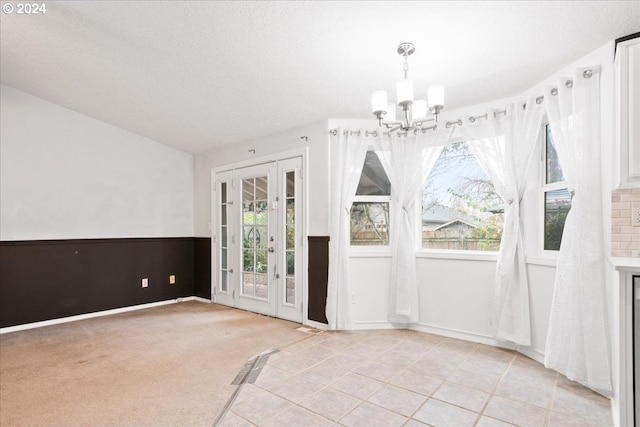 interior space featuring light carpet, french doors, a textured ceiling, and an inviting chandelier