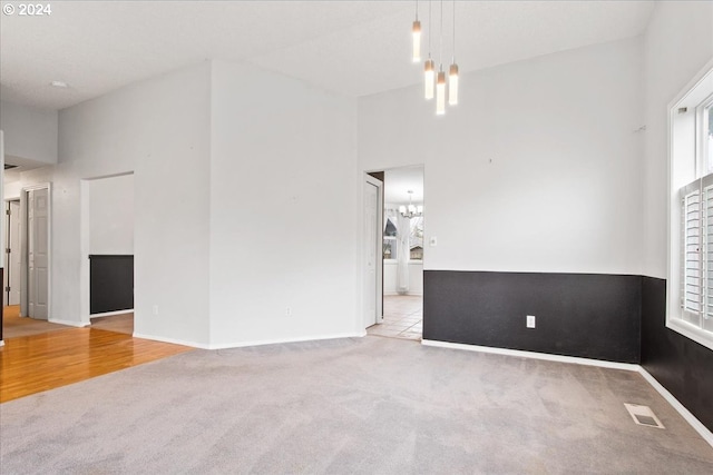 carpeted spare room featuring a high ceiling and a notable chandelier