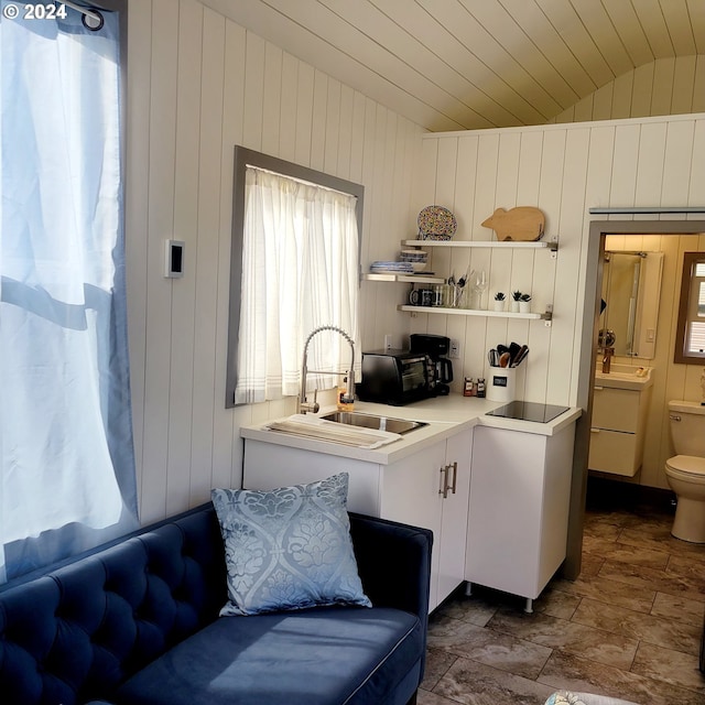 kitchen with sink, vaulted ceiling, wooden walls, black electric stovetop, and white cabinets