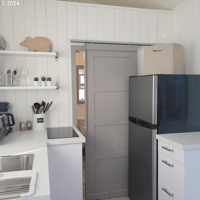 kitchen with white cabinets, stainless steel fridge, black electric cooktop, and wooden walls