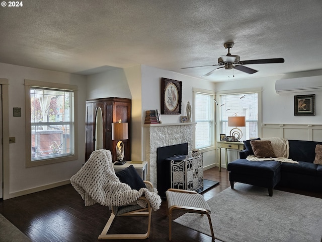 living room featuring a stone fireplace, ceiling fan, dark hardwood / wood-style floors, a textured ceiling, and a wall unit AC