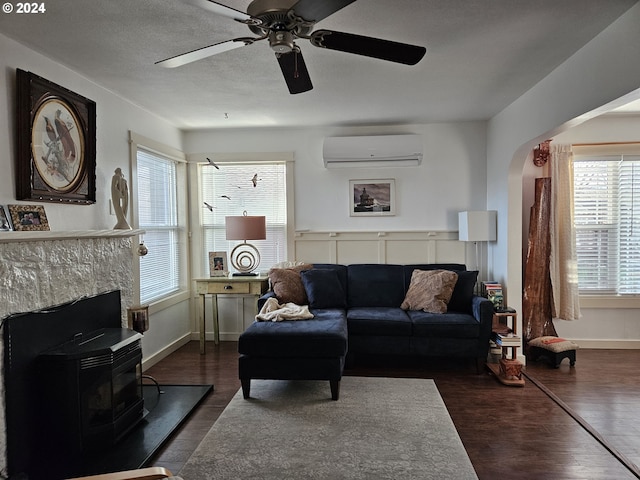 living room with a wall unit AC, a wood stove, ceiling fan, and dark hardwood / wood-style floors