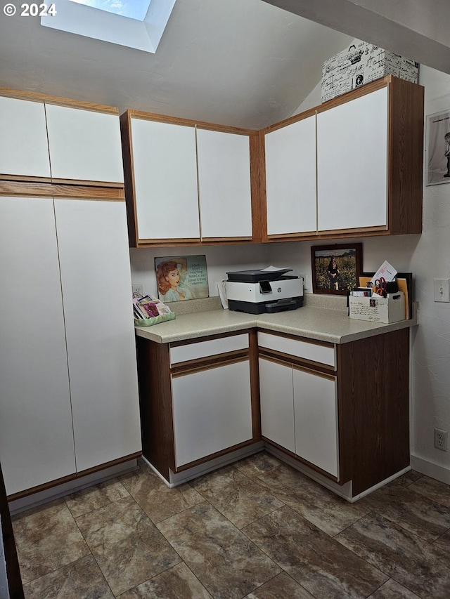 kitchen with vaulted ceiling with skylight and white cabinets