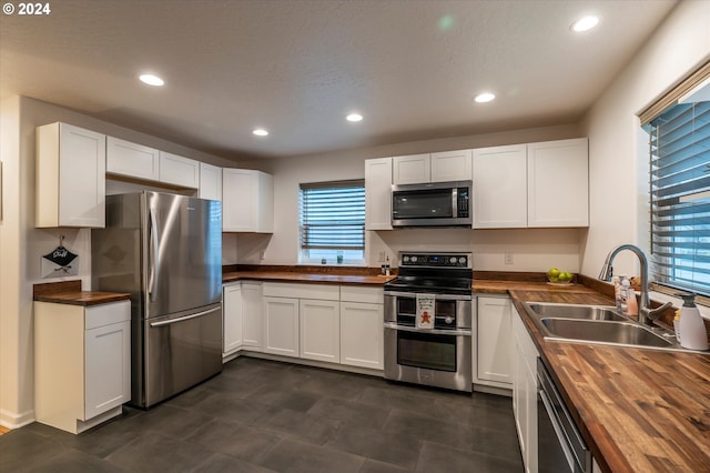 kitchen with white cabinets, butcher block counters, stainless steel appliances, a sink, and recessed lighting