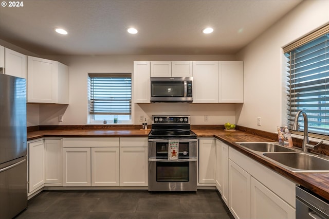 kitchen with recessed lighting, stainless steel appliances, a sink, wood counters, and white cabinets