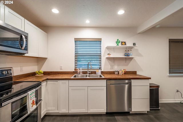 kitchen with stainless steel appliances, butcher block countertops, a sink, and white cabinetry