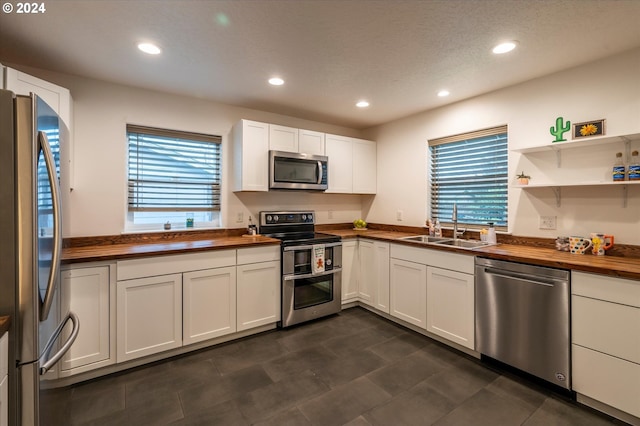 kitchen with wooden counters, appliances with stainless steel finishes, open shelves, and a sink