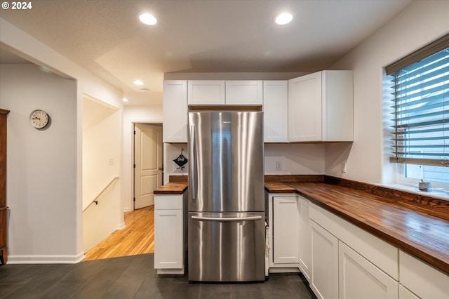 kitchen featuring butcher block counters, freestanding refrigerator, and white cabinets