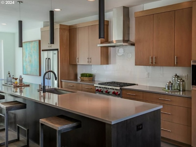 kitchen with sink, high quality appliances, wall chimney exhaust hood, decorative backsplash, and a breakfast bar area