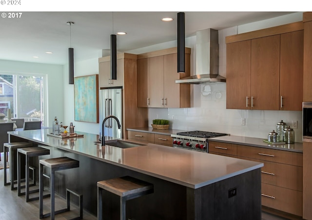 kitchen with a kitchen island with sink, wall chimney exhaust hood, a kitchen breakfast bar, wood-type flooring, and sink