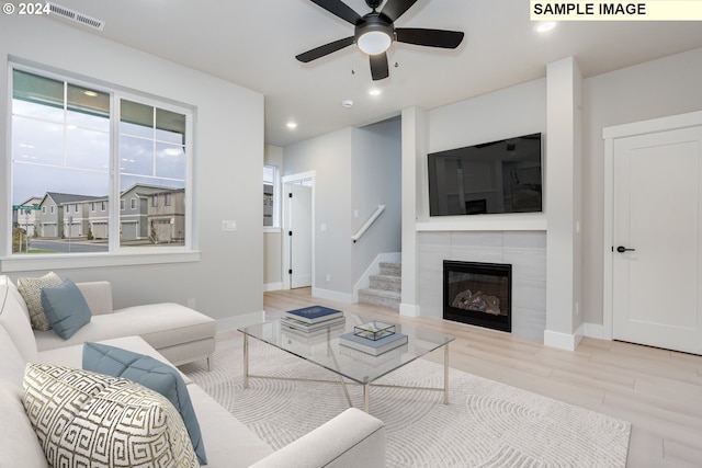 living room with ceiling fan, light hardwood / wood-style floors, and a tiled fireplace