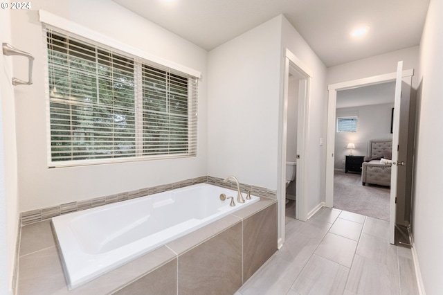 bathroom featuring tiled tub, tile patterned flooring, and toilet