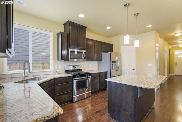 kitchen featuring light stone counters, stainless steel appliances, sink, and hanging light fixtures