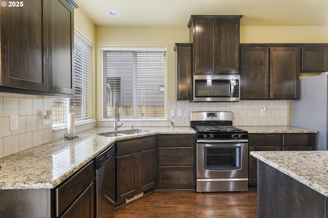 kitchen with stainless steel appliances, dark hardwood / wood-style flooring, light stone countertops, and sink