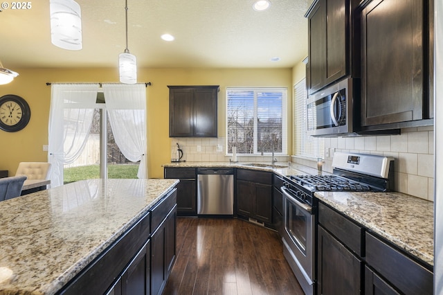 kitchen featuring appliances with stainless steel finishes, dark hardwood / wood-style floors, hanging light fixtures, light stone countertops, and dark brown cabinets