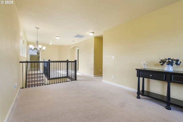 spare room featuring an inviting chandelier, light colored carpet, and a textured ceiling