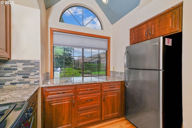 kitchen featuring tasteful backsplash, light stone counters, stainless steel appliances, vaulted ceiling, and light hardwood / wood-style floors