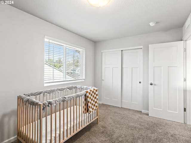 bedroom with a nursery area, a textured ceiling, a closet, and carpet