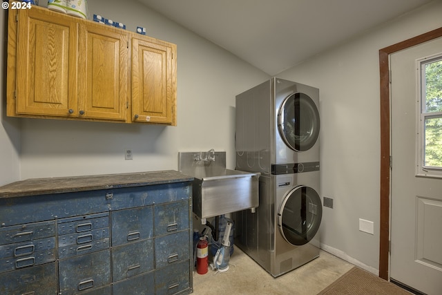 clothes washing area featuring a wealth of natural light, sink, cabinets, and stacked washer / drying machine