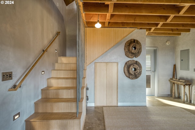 stairway featuring electric panel, beam ceiling, and a high ceiling