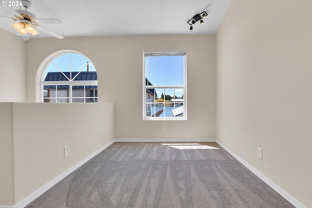 spare room featuring a water view, carpet, track lighting, and ceiling fan