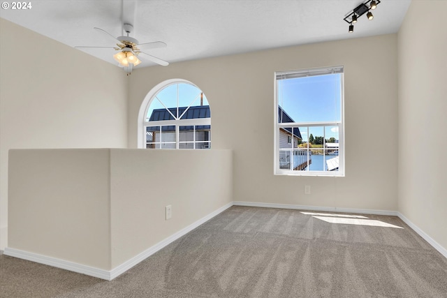 empty room featuring track lighting, ceiling fan, and carpet flooring