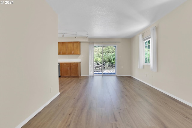 unfurnished living room featuring light hardwood / wood-style flooring, rail lighting, and a textured ceiling