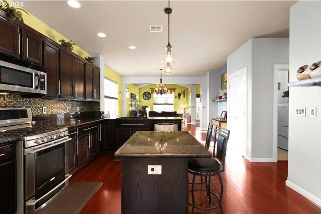 kitchen with a kitchen breakfast bar, dark stone countertops, decorative light fixtures, dark hardwood / wood-style flooring, and stainless steel appliances