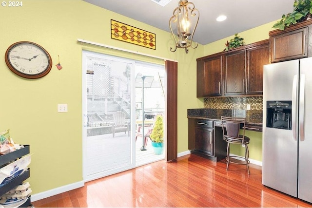 kitchen with hanging light fixtures, stainless steel refrigerator with ice dispenser, hardwood / wood-style floors, decorative backsplash, and dark brown cabinets