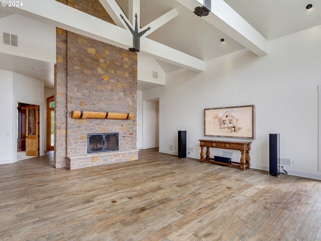 unfurnished living room with light wood-type flooring, high vaulted ceiling, beam ceiling, and a stone fireplace