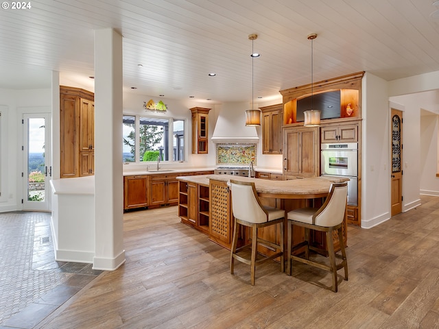 kitchen with a kitchen island with sink, light wood-type flooring, custom range hood, and plenty of natural light