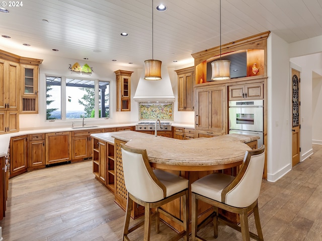 kitchen with hanging light fixtures, custom range hood, light hardwood / wood-style flooring, stainless steel appliances, and a breakfast bar area