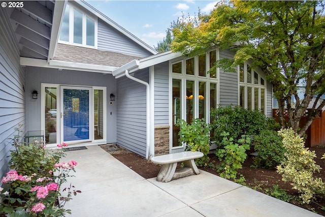 entrance to property with stone siding, a shingled roof, and a patio