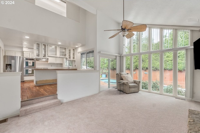 unfurnished living room with a towering ceiling, light colored carpet, and ceiling fan