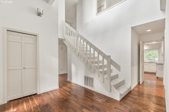 entrance foyer with beam ceiling, a stone fireplace, high vaulted ceiling, and dark wood-type flooring