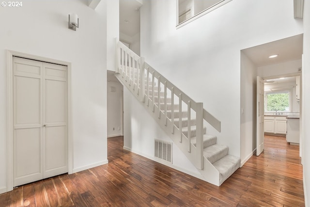 stairway with hardwood / wood-style floors and a towering ceiling