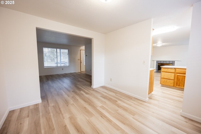 unfurnished room featuring a tiled fireplace and light wood-type flooring