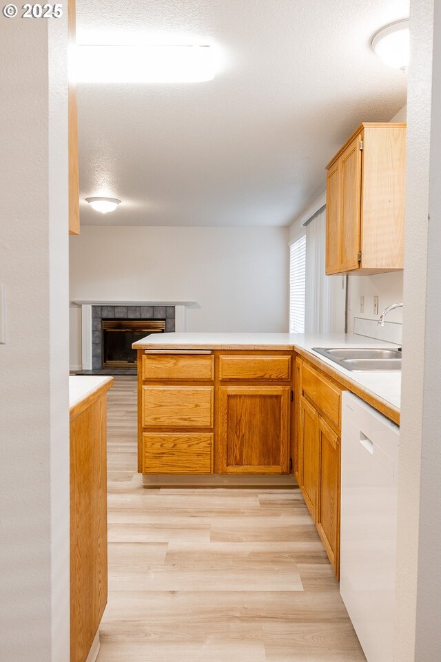 kitchen featuring white dishwasher, a tile fireplace, sink, light wood-type flooring, and kitchen peninsula