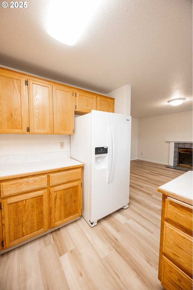 kitchen featuring white fridge with ice dispenser, light hardwood / wood-style flooring, a textured ceiling, and a fireplace