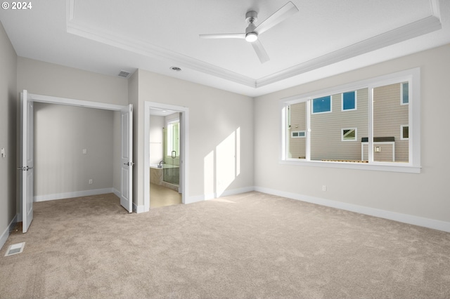 unfurnished bedroom with a tray ceiling, ensuite bath, and ceiling fan