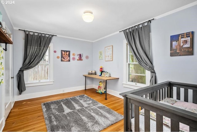 bedroom with wood-type flooring, a crib, ornamental molding, and multiple windows