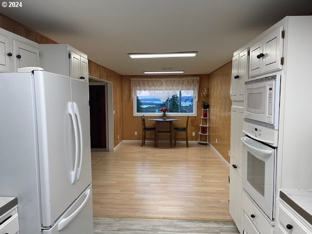 kitchen featuring wooden walls, white appliances, white cabinetry, and light wood-type flooring