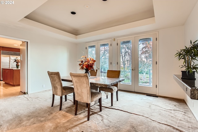 carpeted dining area featuring a raised ceiling, french doors, and a healthy amount of sunlight