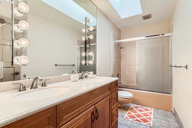 full bathroom featuring a skylight, bath / shower combo with glass door, vanity, tile patterned flooring, and toilet