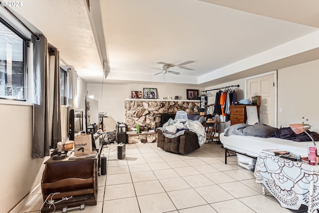 tiled bedroom featuring a tray ceiling, a stone fireplace, and ceiling fan