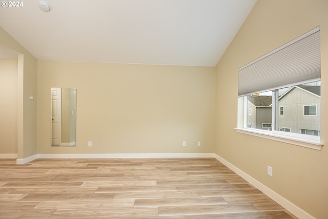 spare room featuring vaulted ceiling, baseboards, and light wood-type flooring