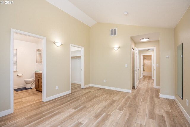 unfurnished bedroom featuring light wood-type flooring, ensuite bath, a spacious closet, a closet, and lofted ceiling